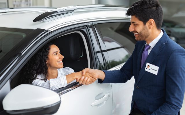 Happy business woman buying new luxury auto in showroom Happy young business woman buying new luxury auto in new showroom, shaking middle-eastern man sales assistant hand and smiling, closeup. Car purchasing, automobile leasing concept
